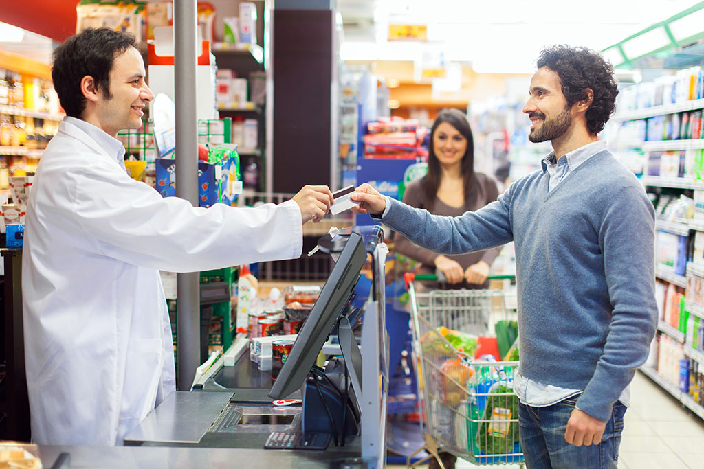 SENOR_A man checks out by create card at the counter through a POS machine at a pharmacy.